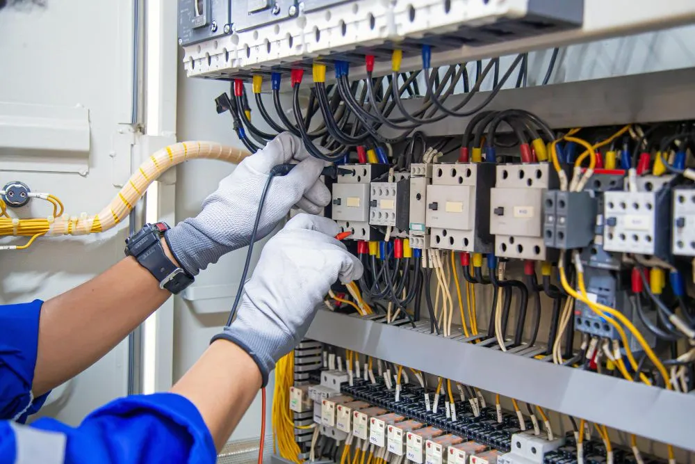 Gloved electrician checking voltage on contactors and wiring in a main distribution board