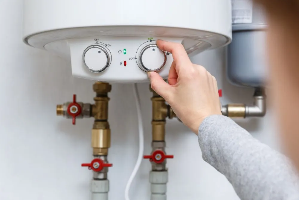 Hand adjusting the thermostat dial on an electric tank water heater