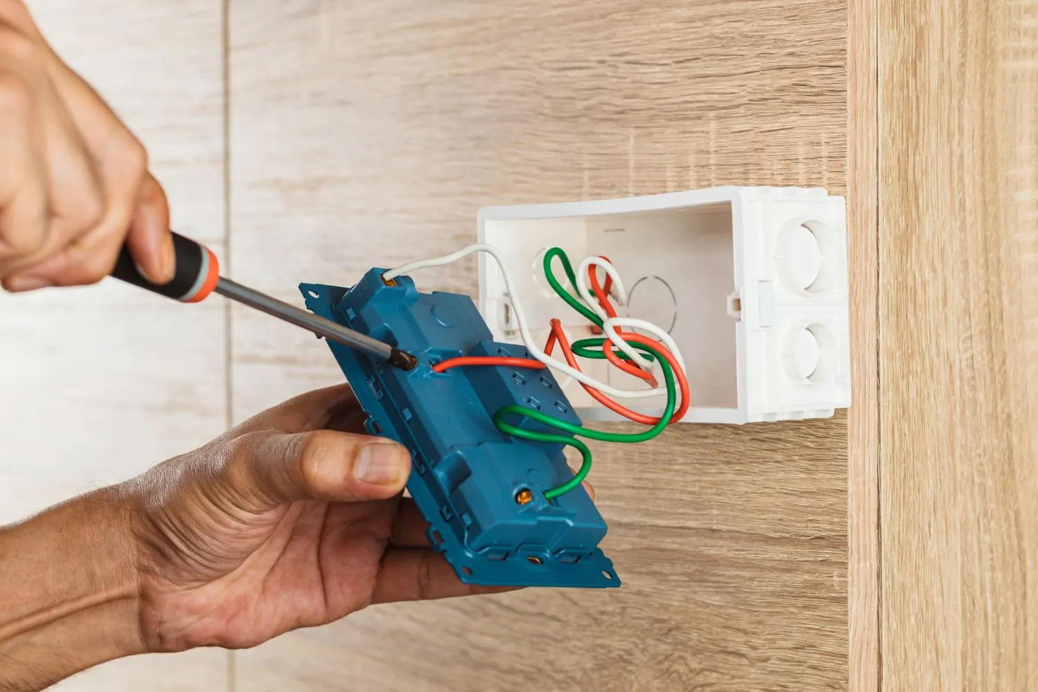 Electrician using a screwdriver to attach wires to a wall outlet