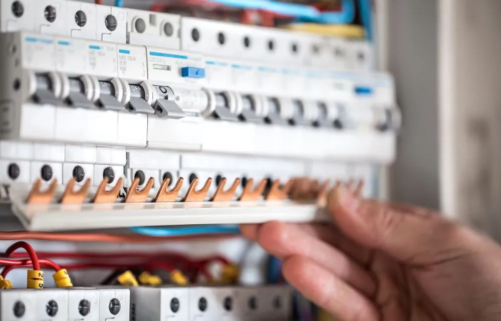 Hand fitting a busbar across a row of circuit breakers in an electrical panel